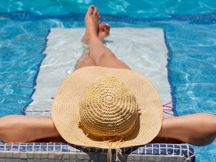 Kvinna i solhatt som njuter i solen i grund pool