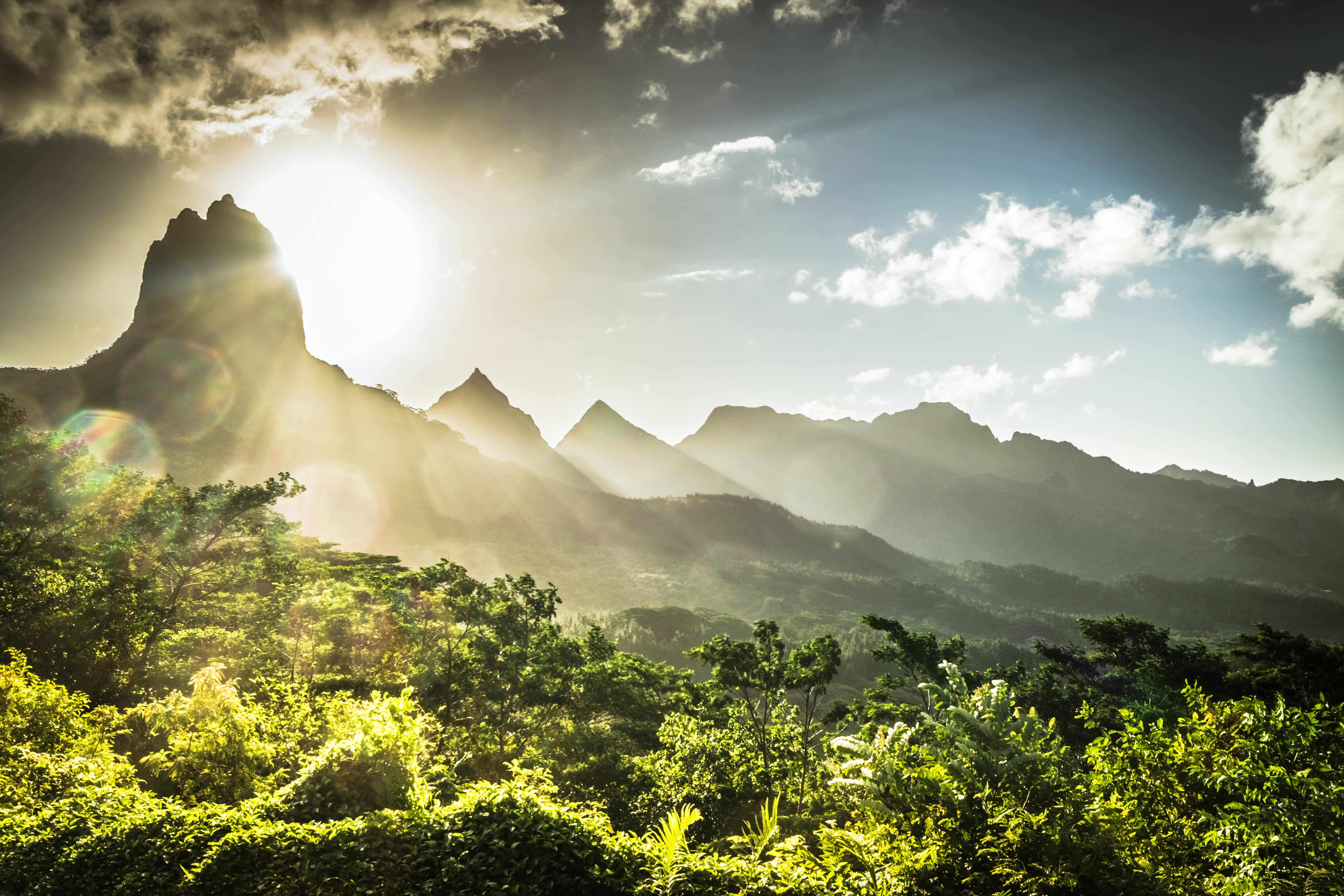 Solen står lågt bakom de gröna bergen på Moorea