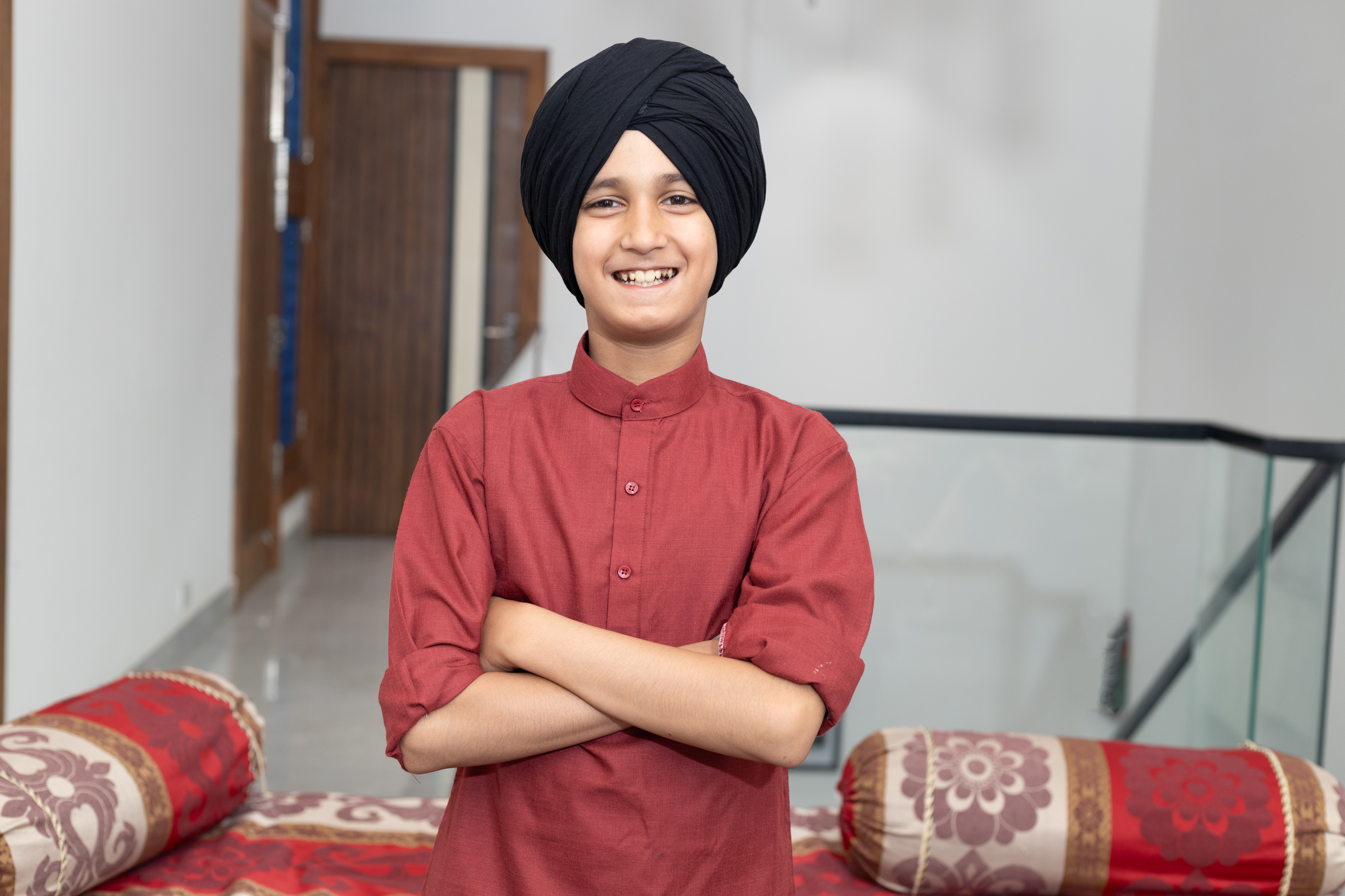 En ung indisk sikh-dreng står med korslagte arme i hjemlige omgivelser – med rødder i Punjabs kultur og sikhismen