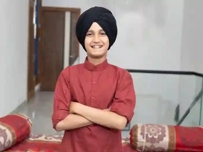 En ung indisk sikh-dreng står med korslagte arme i hjemlige omgivelser – med rødder i Punjabs kultur og sikhismen