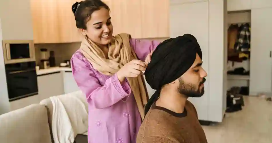 Ung, glad og smilende indisk kvinde sætter en turban på sin mand