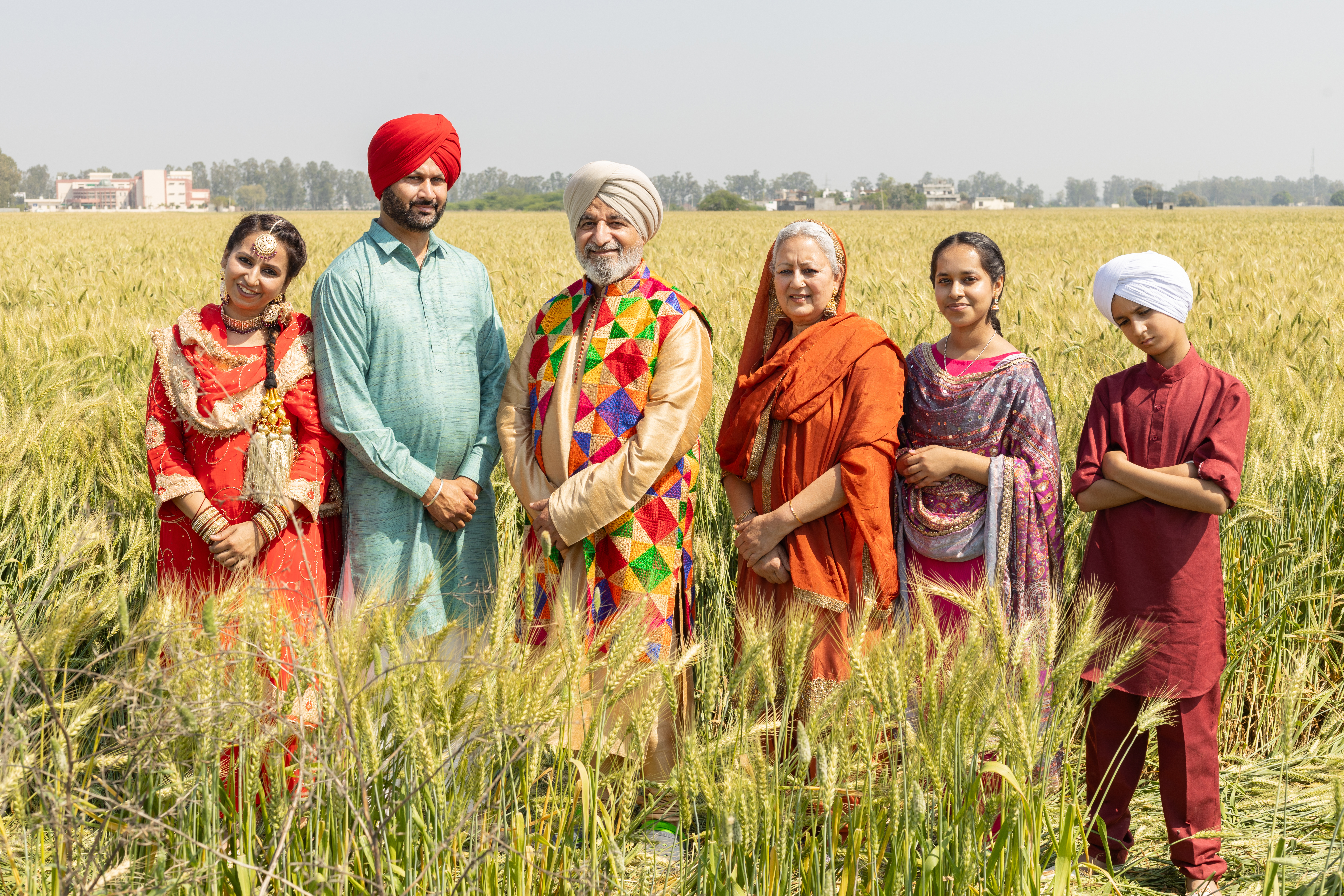 En punjabisk sikh-familie står sammen ude ved en mark iført farverigt tøj. Folk fra Punjab og Indiens kultur