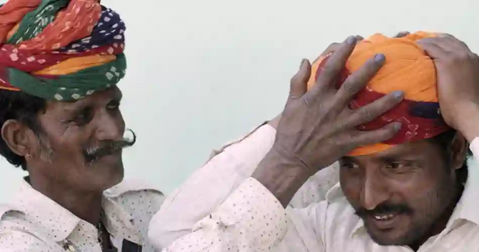 En smilende ældre mand fra Sydasien hjælper sin søn med at tage turbanen på