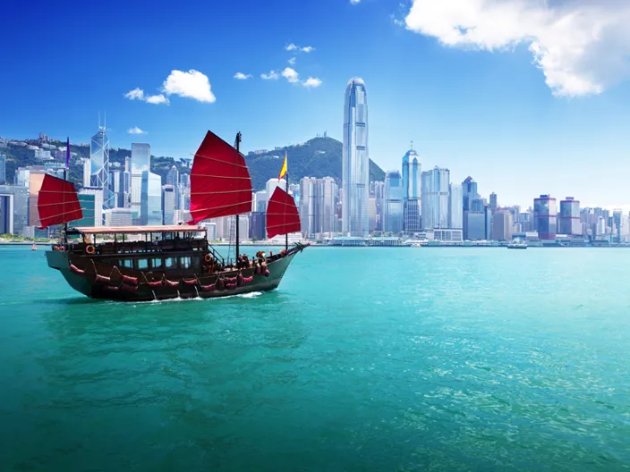 En klassisk träbåt seglar framför Hongkongs moderna skyline.