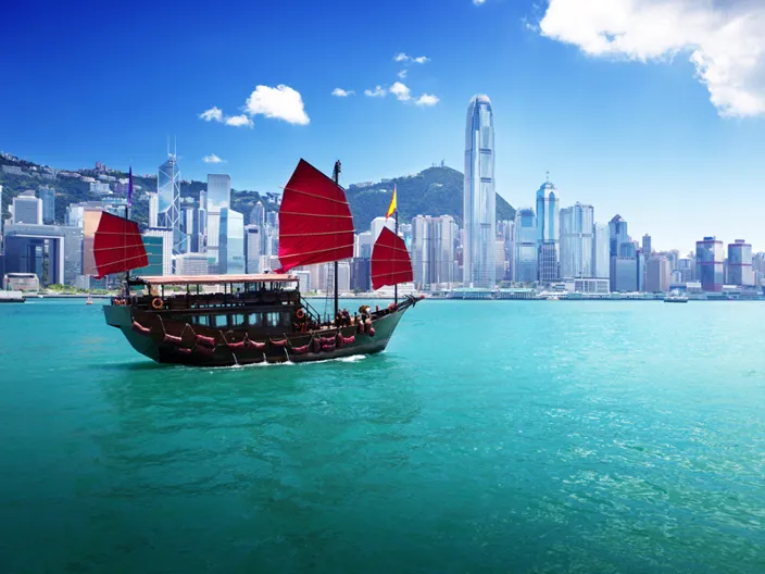 En klassisk träbåt seglar framför Hongkongs moderna skyline.